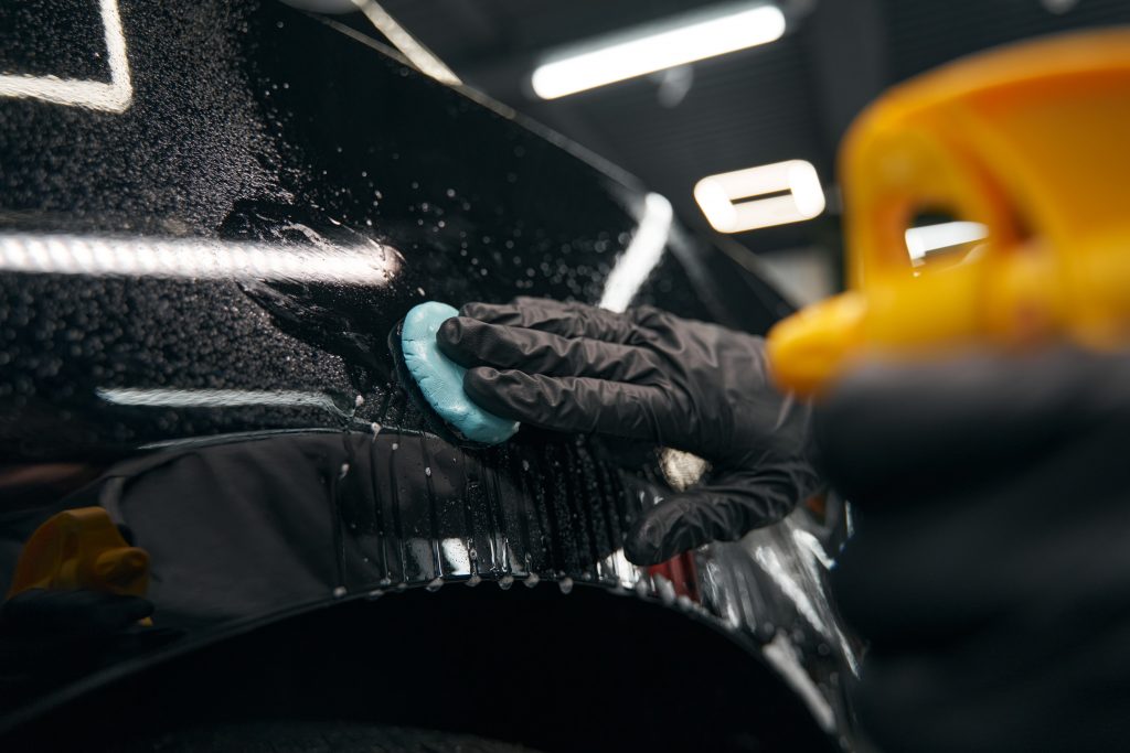Cropped photo of skilled worker in nitrile gloves pressing lump of clay to car surface